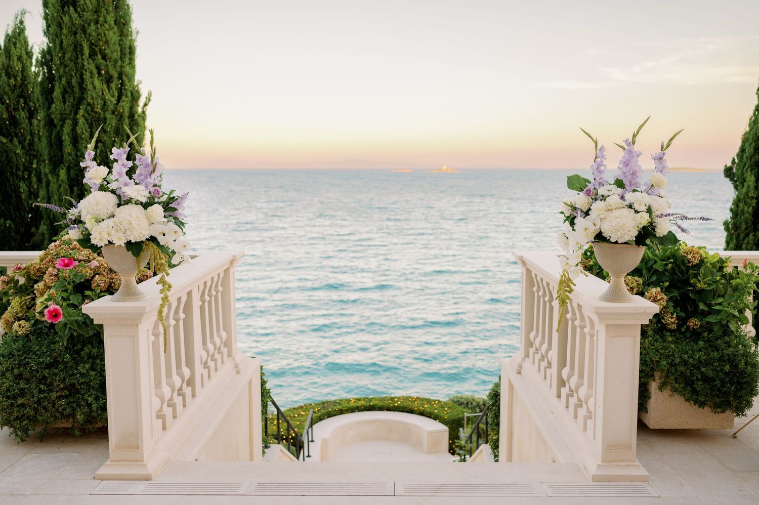 Oceanfront wedding ceremony setup with white floral arrangements and stone balustrade.