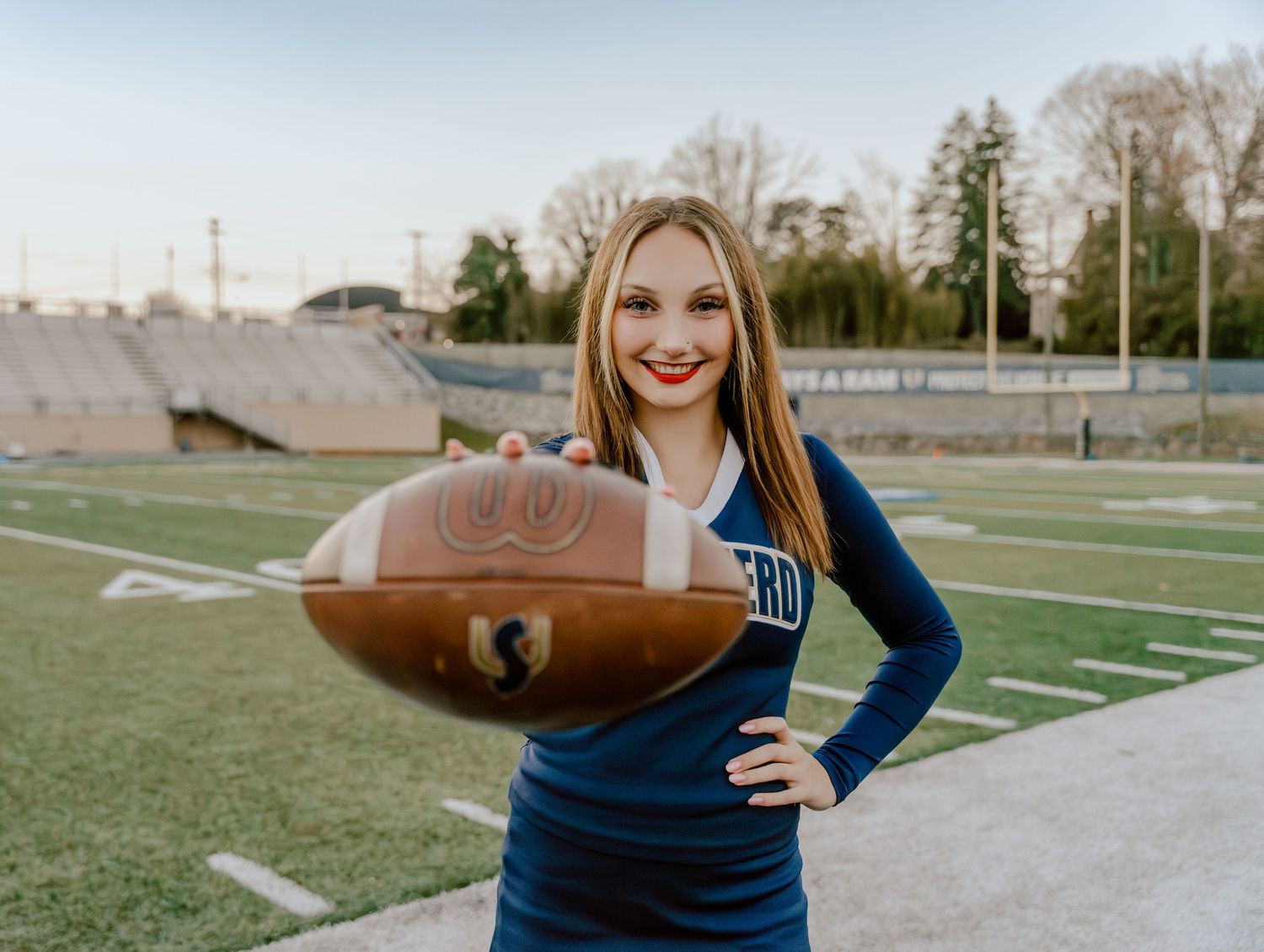 Football player in blue uniform posing with ball on sports field.