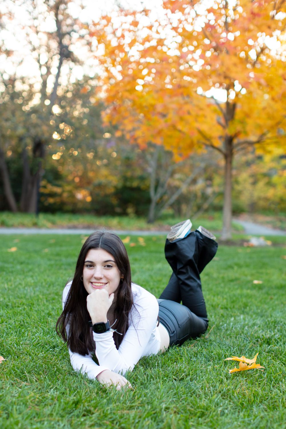 Person in black clothing lying on grass with vibrant fall foliage in background.