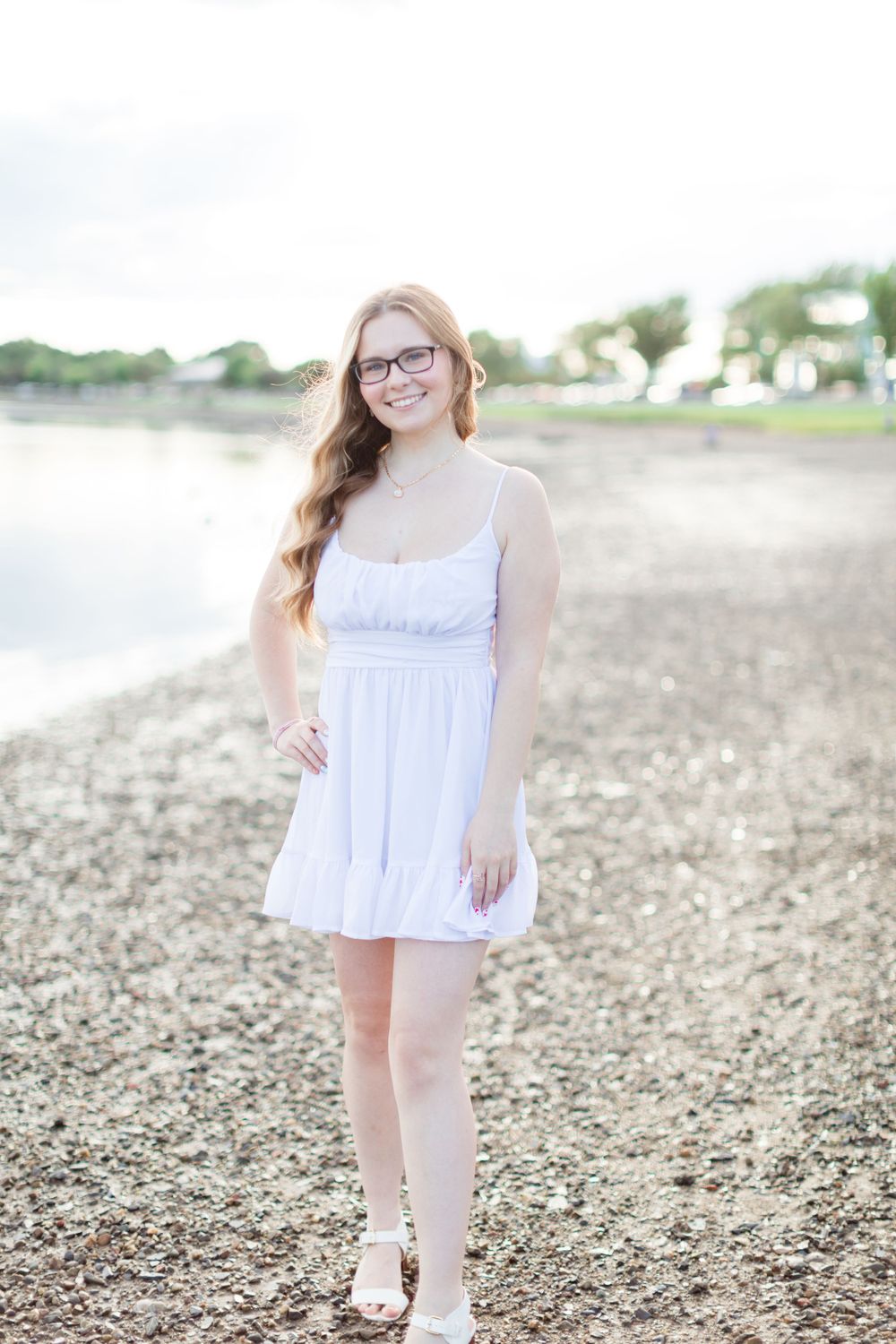 Person in white dress standing on rocky beach shore at sunset.