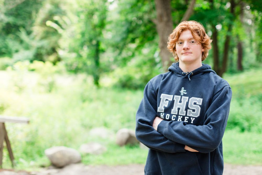 Person wearing navy blue FHS sweatshirt in outdoor woodland setting.