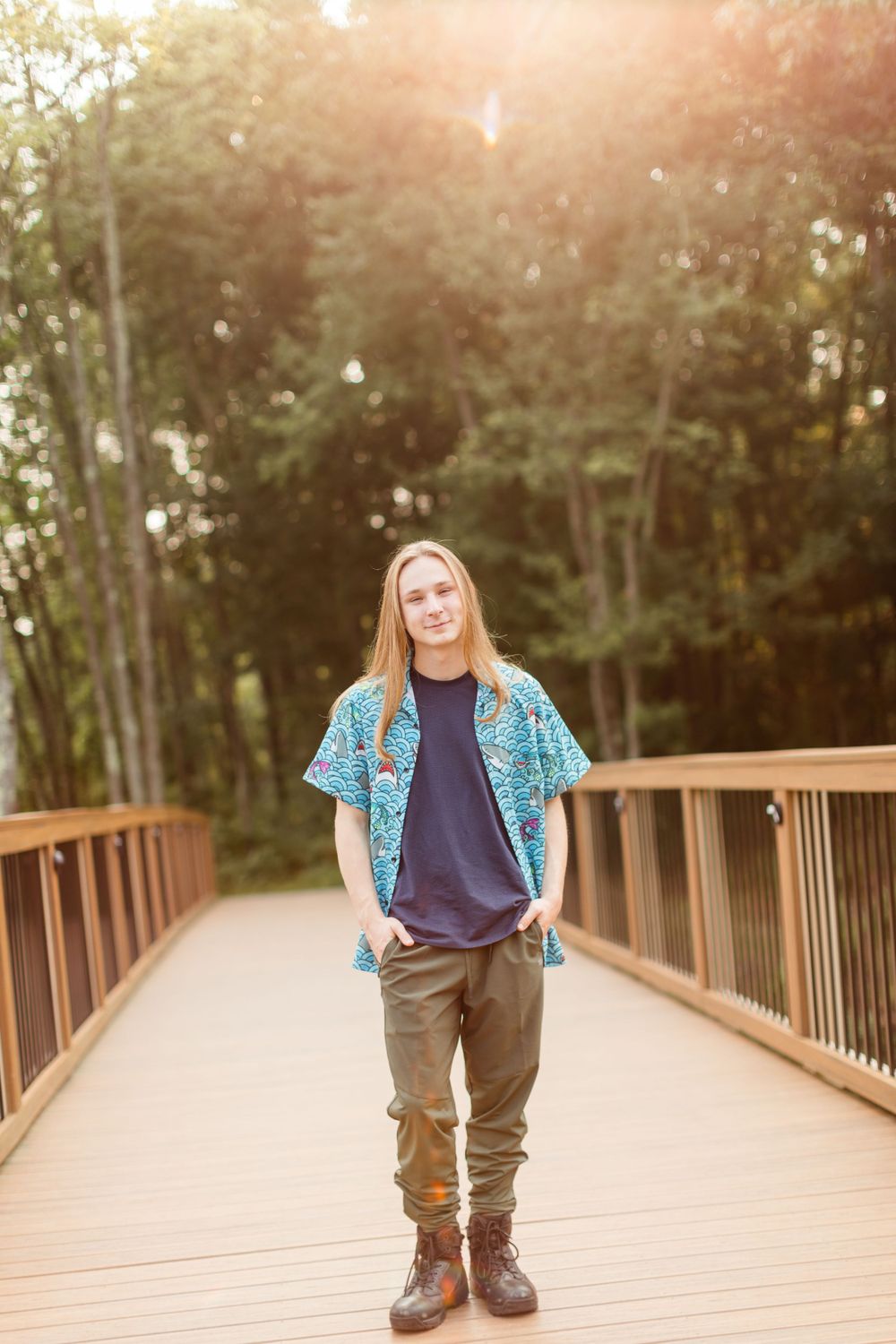 Person in teal shirt and brown pants standing on wooden bridge at sunset.
