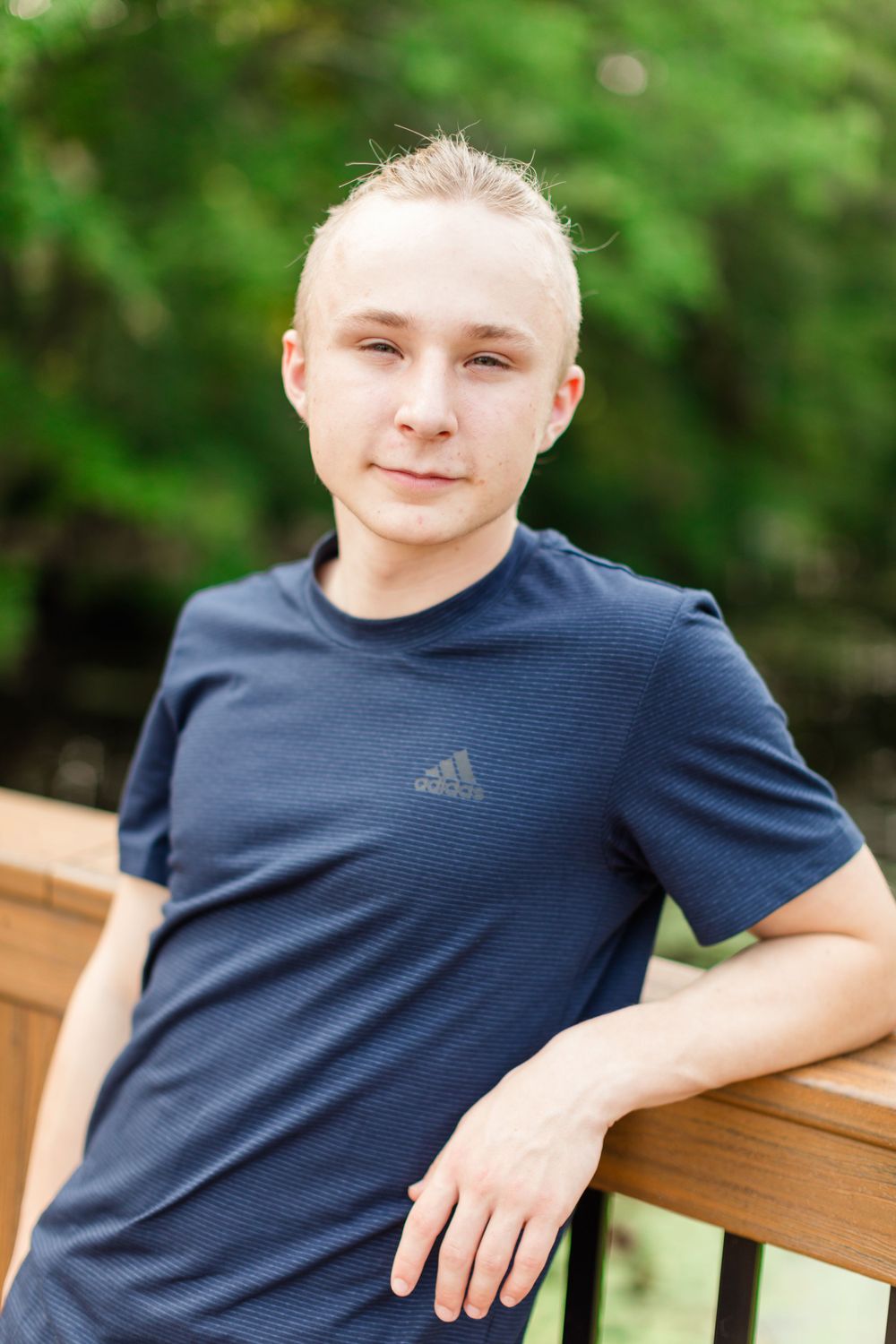 Portrait in navy Adidas shirt against wooden railing outdoors.