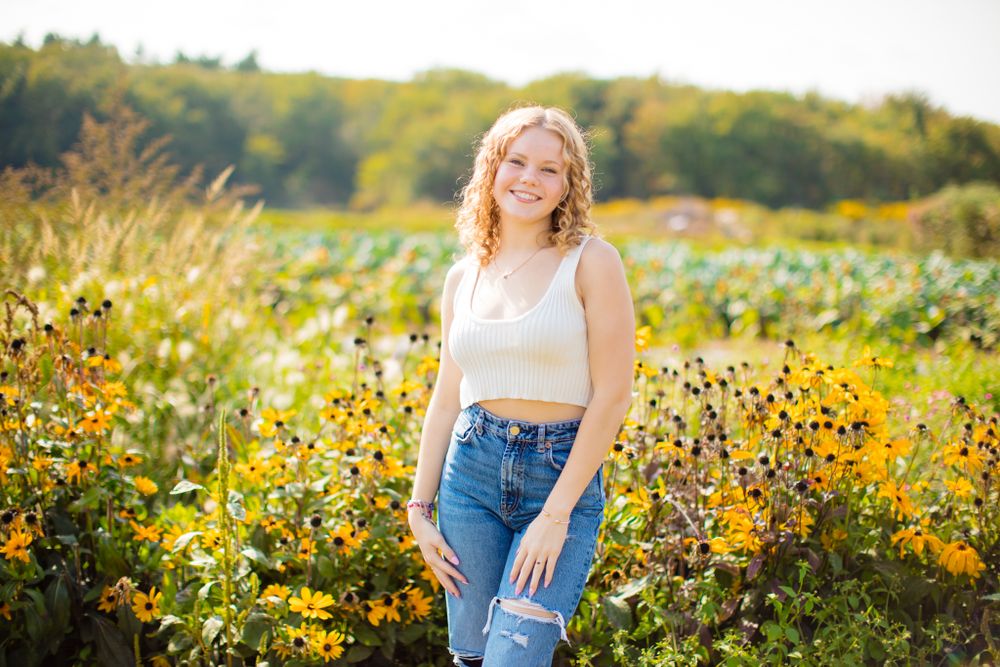 Person in white top and jeans standing in field of yellow wildflowers at golden hour.