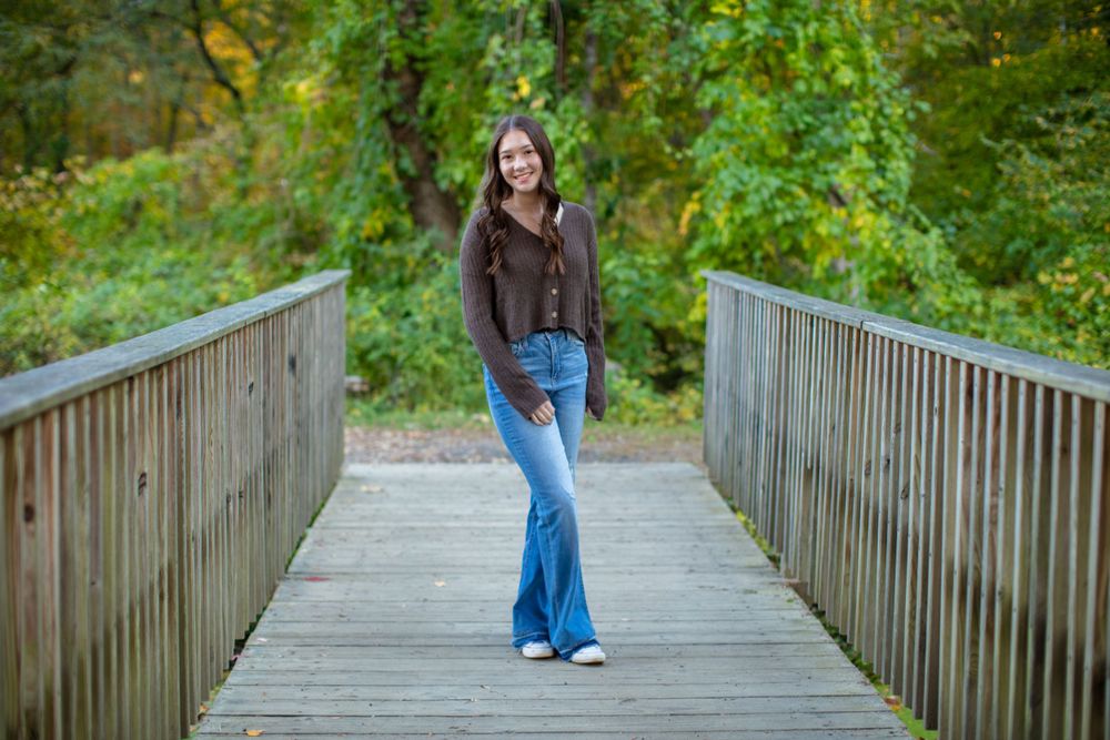 A figure stands on a wooden bridge walkway surrounded by vibrant autumn foliage in natural lighting.