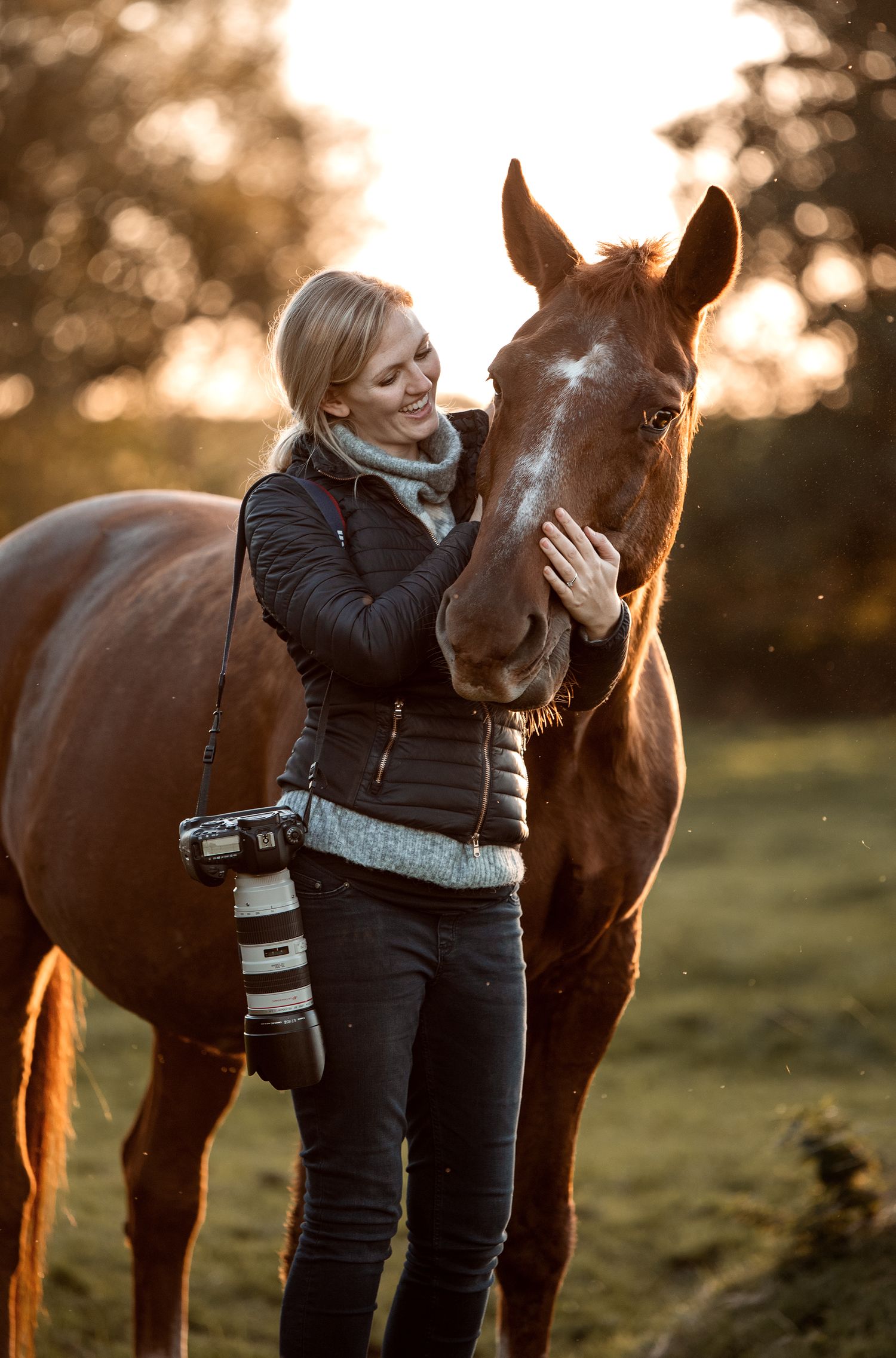 Intimate bonding moment between rider and chestnut horse at golden sunset with camera equipment visible.