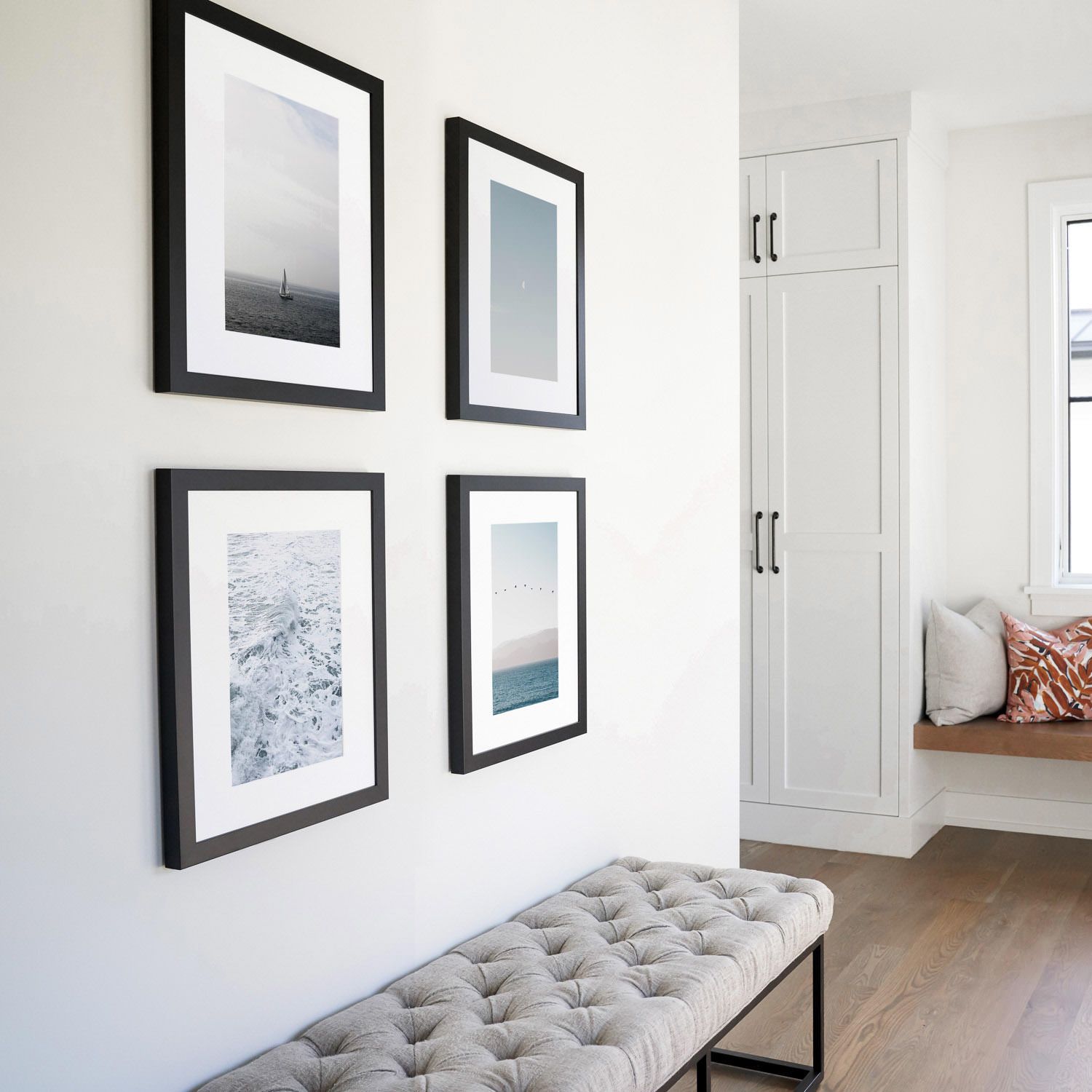 Four black-framed landscape photographs arranged in a grid on white wall above grey bench.