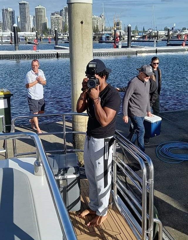 Group of photographers and people on dock near marina with city skyline in background.