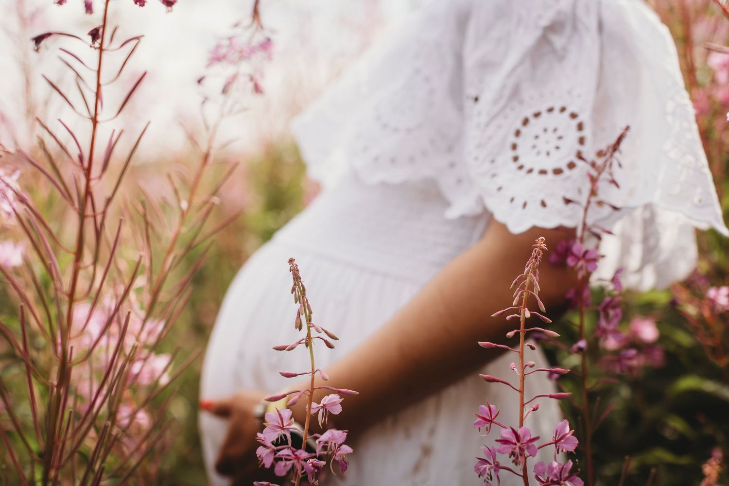 Close up of a white lace dress among pink wildflowers in a garden setting.