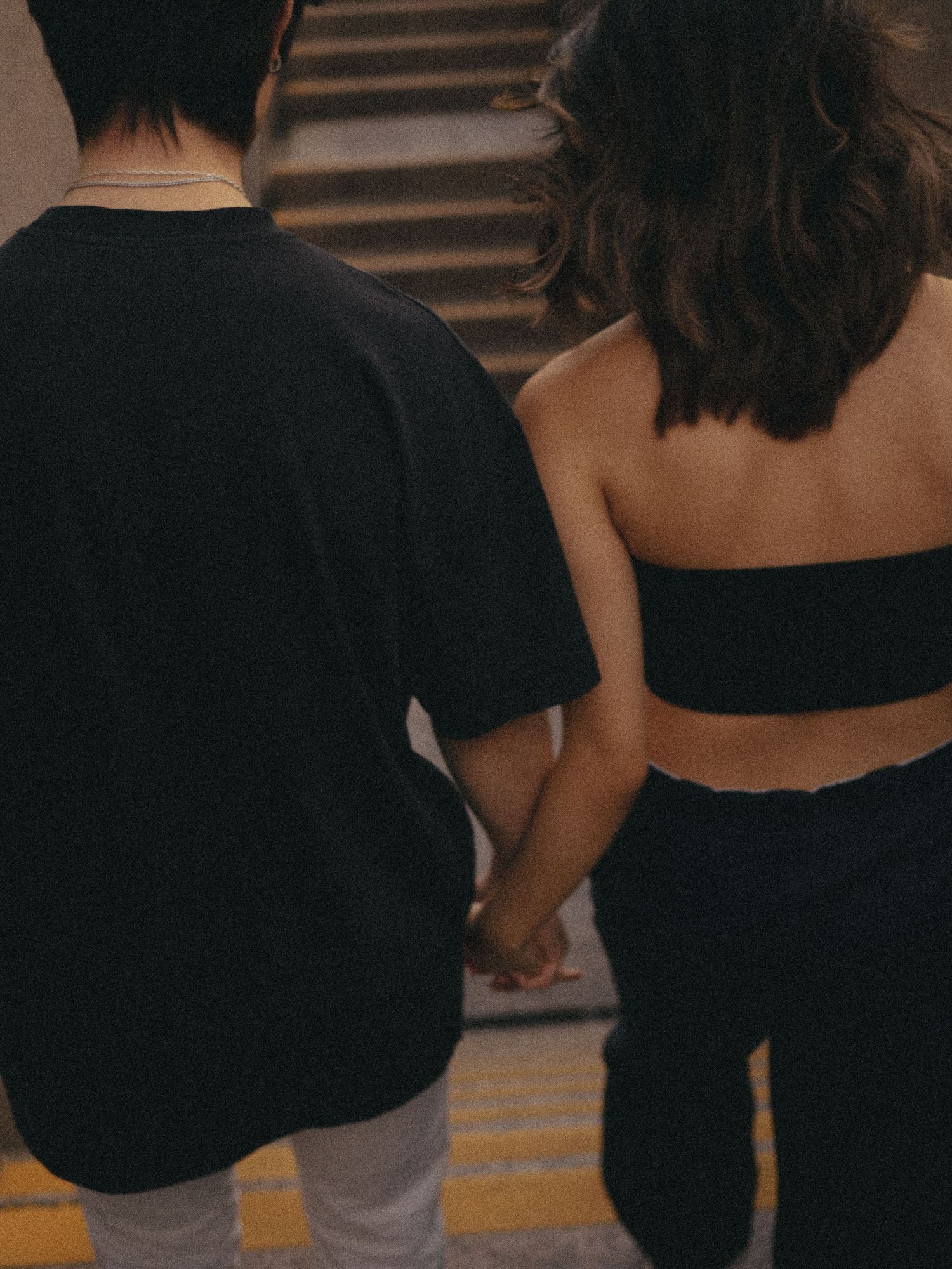 Two people holding hands while ascending stairs in dark atmospheric lighting.