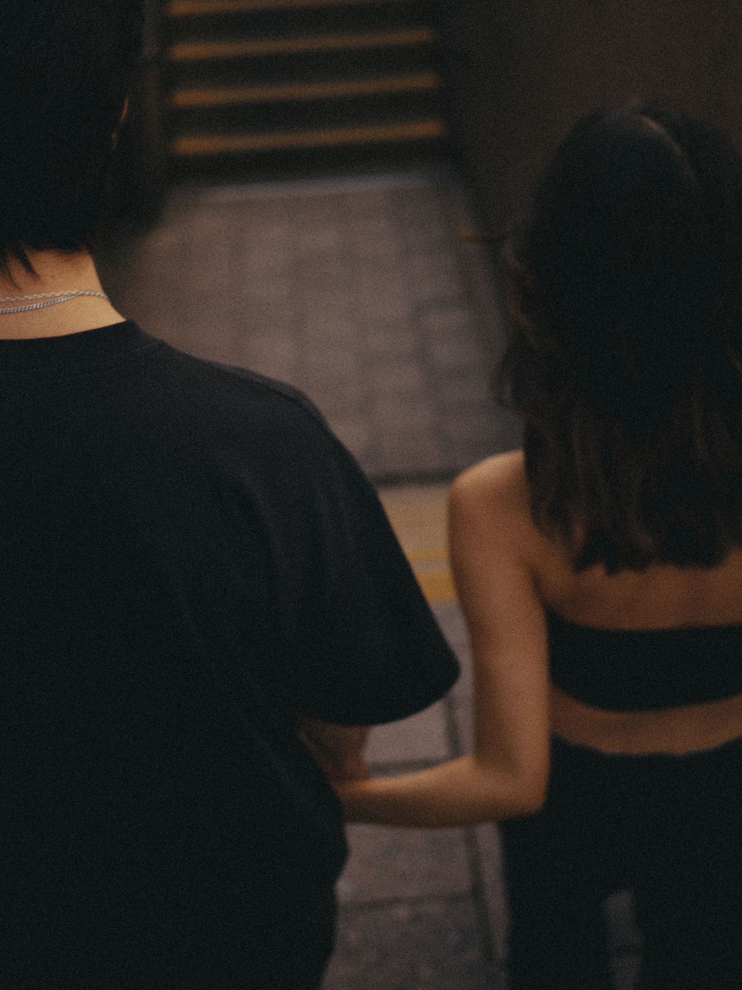 Couple in dark clothing walking together up dimly lit stairs.