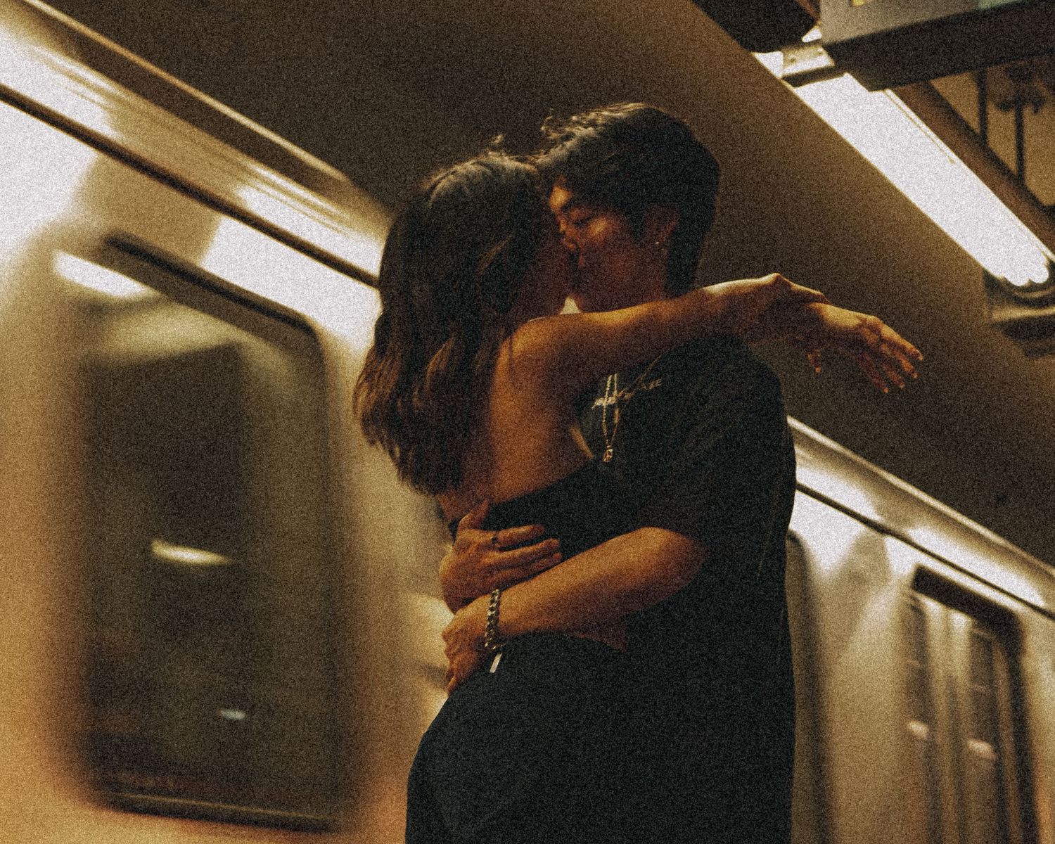 Intimate couple embrace against subway train interior in warm lighting.