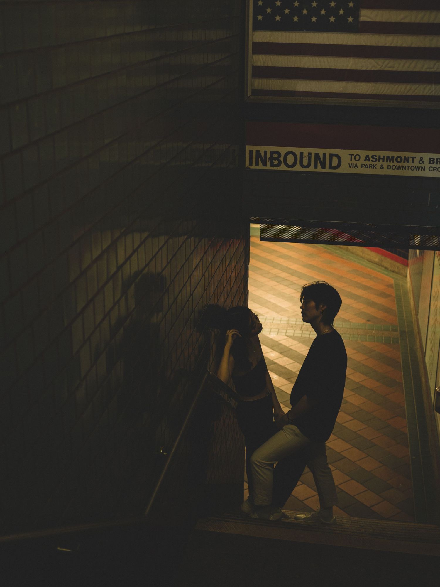 Silhouette in subway station with American flag and 'Inbound' sign visible.