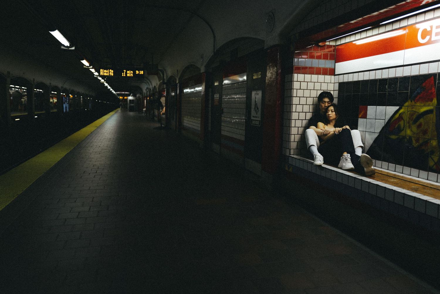 Empty subway platform with lone figure silhouetted against illuminated station window.