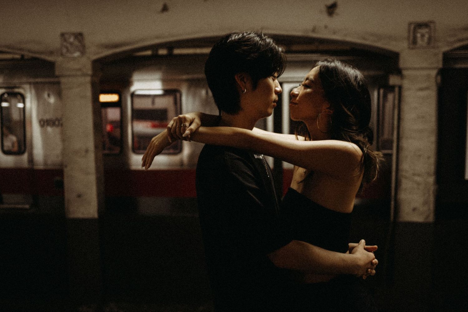 Couple sharing tender embrace in vintage-toned subway station setting.