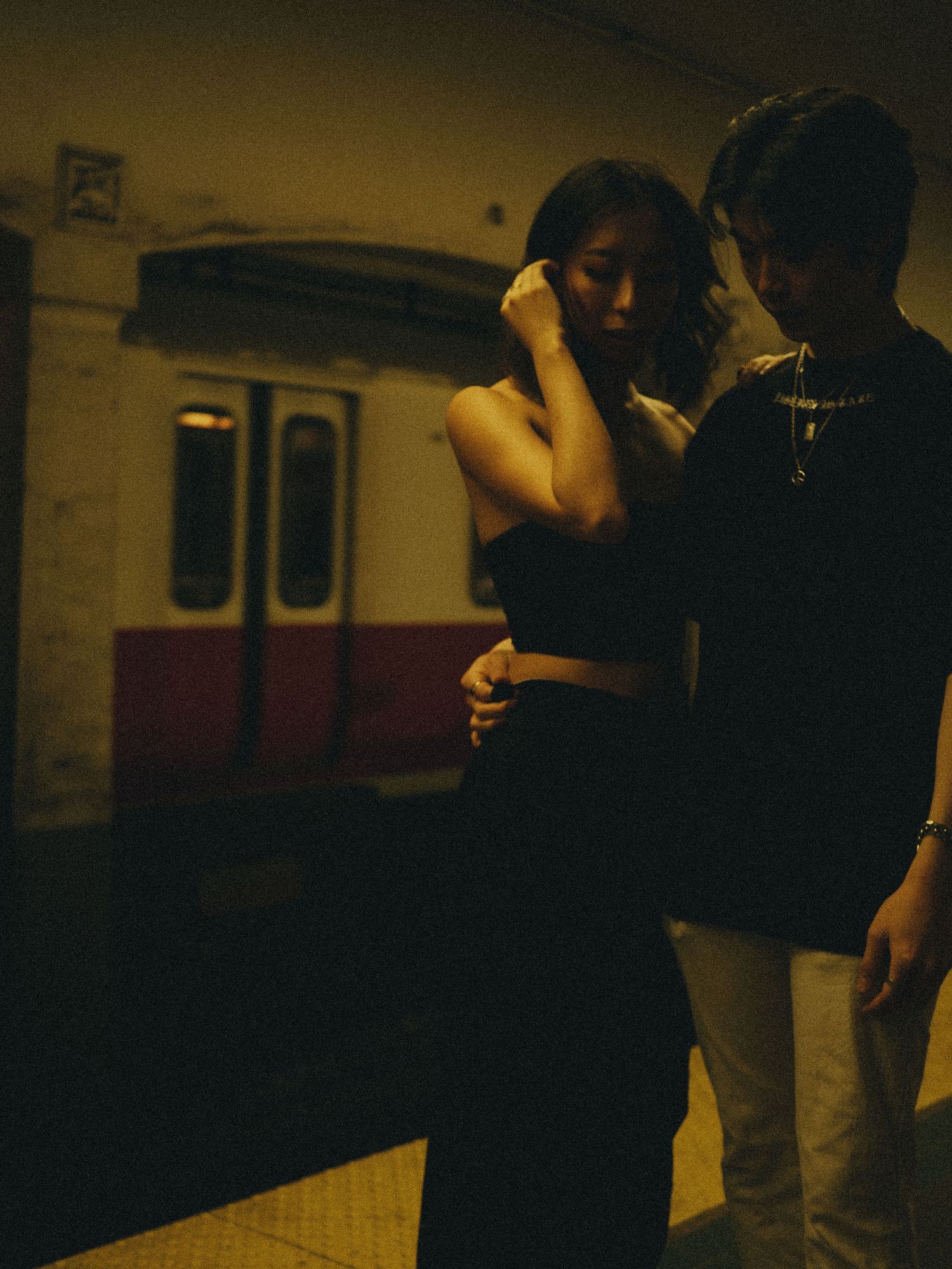 Romantic couple embracing in moody lighting at subway station.