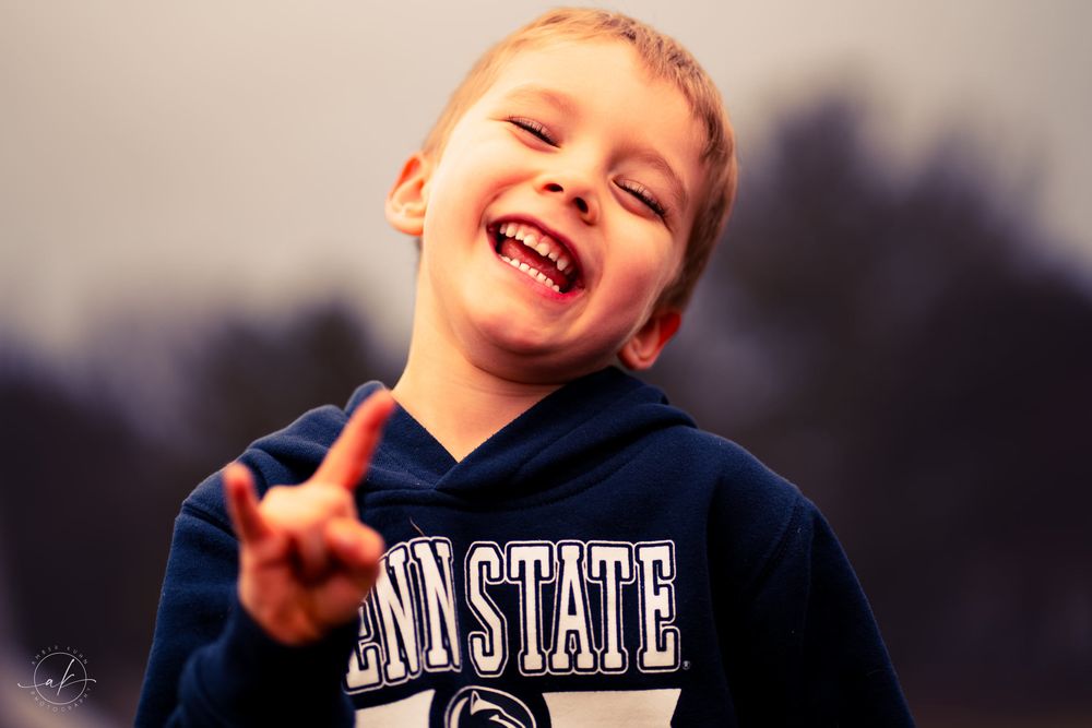 Energetic child in a Penn State hoodie making peace sign with joyful expression.