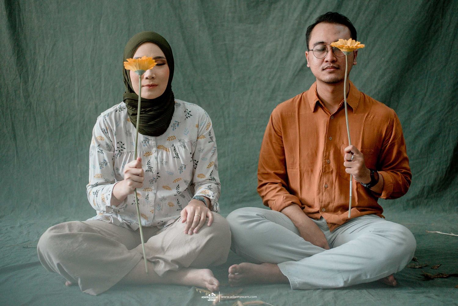 A couple posing with orange slices covering their eyes in a creative studio portrait.