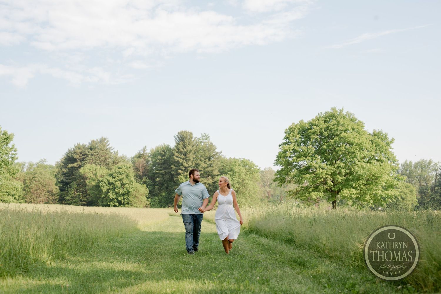 A couple walks hand in hand through a serene meadow on a bright summer day.