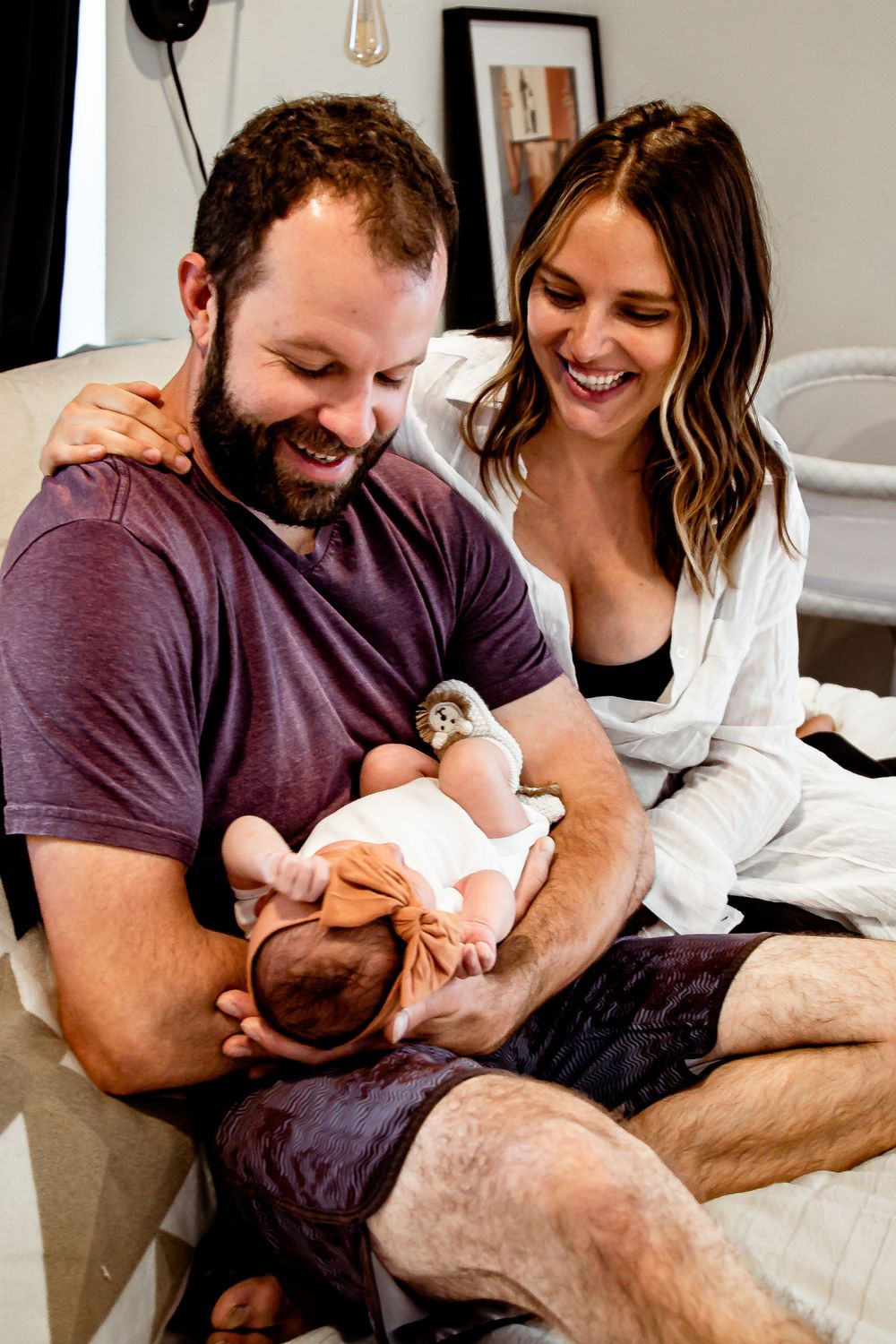 Parents share joyful moment with newborn baby while relaxing on cozy bed. Denver Family Photography.