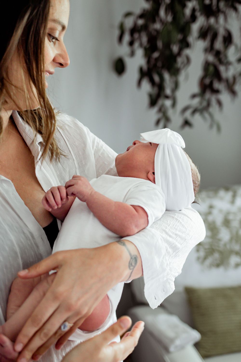 Mother in white shirt tenderly holding newborn baby wrapped in white cloth indoors. Denver Family Photography.