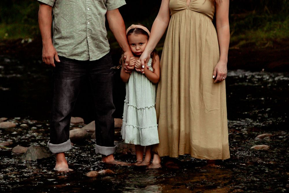 A casual family portrait showing legs and feet standing together in shallow water among rocks. Denver Family Photography.