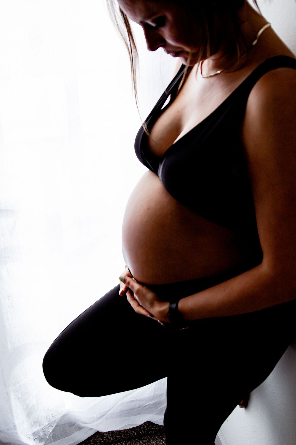 Artistic silhouette of pregnant woman in black against bright window. Denver Family Photography.