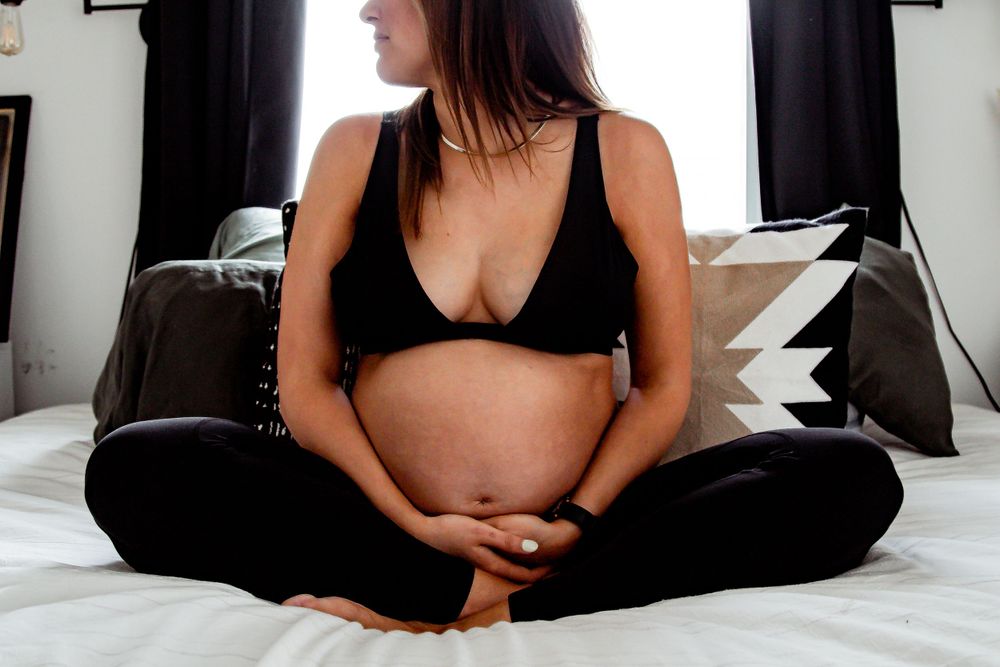 Maternity photo of pregnant belly in black loungewear while sitting on white bedding. Denver Family Photography.