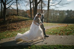 bride and groom hurry along a path, bride's dress flowing around them, with sun flares and bright light around them