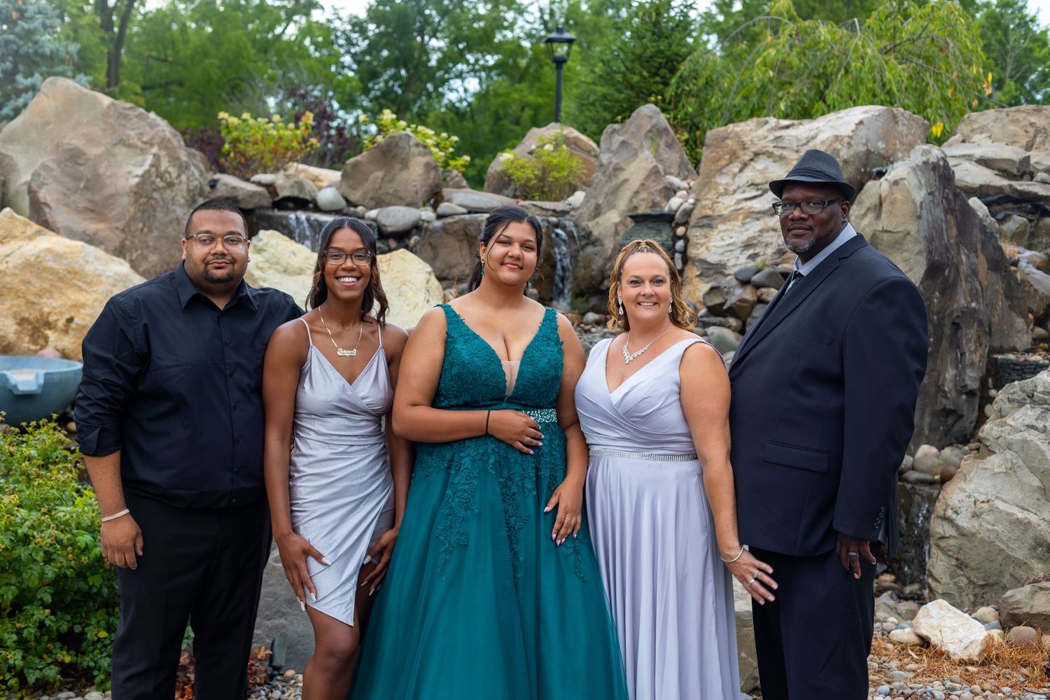 A group of friends pose together outdoors near a rocky landscape wearing formal attire.