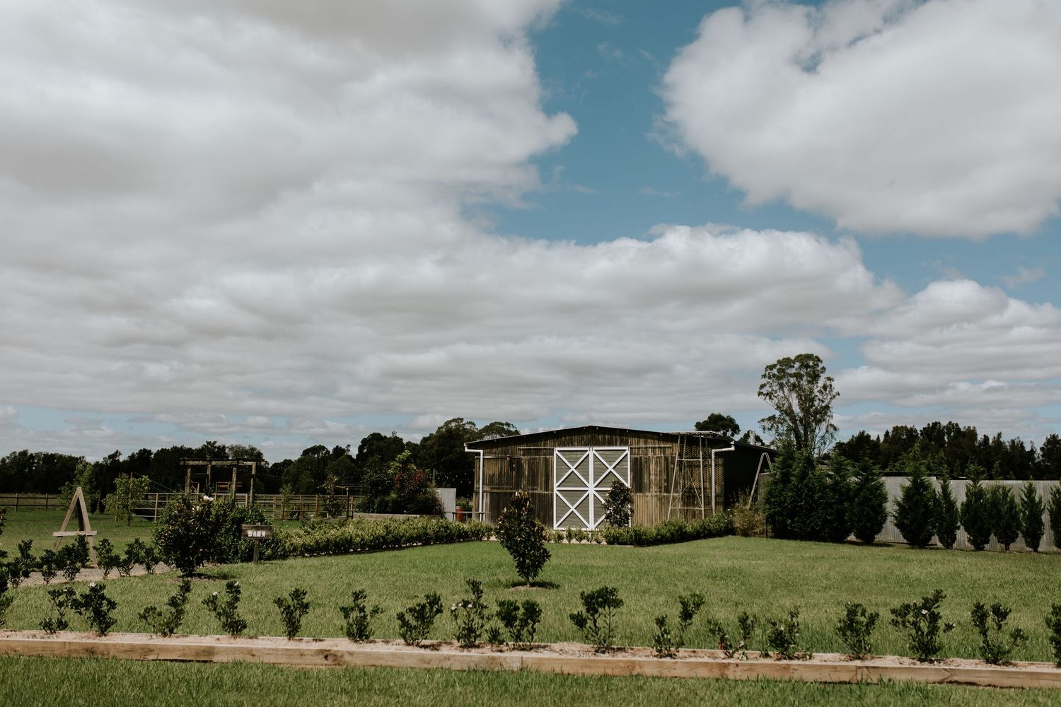 A modern barn-style wedding venue set on rolling hills under cloudy skies.