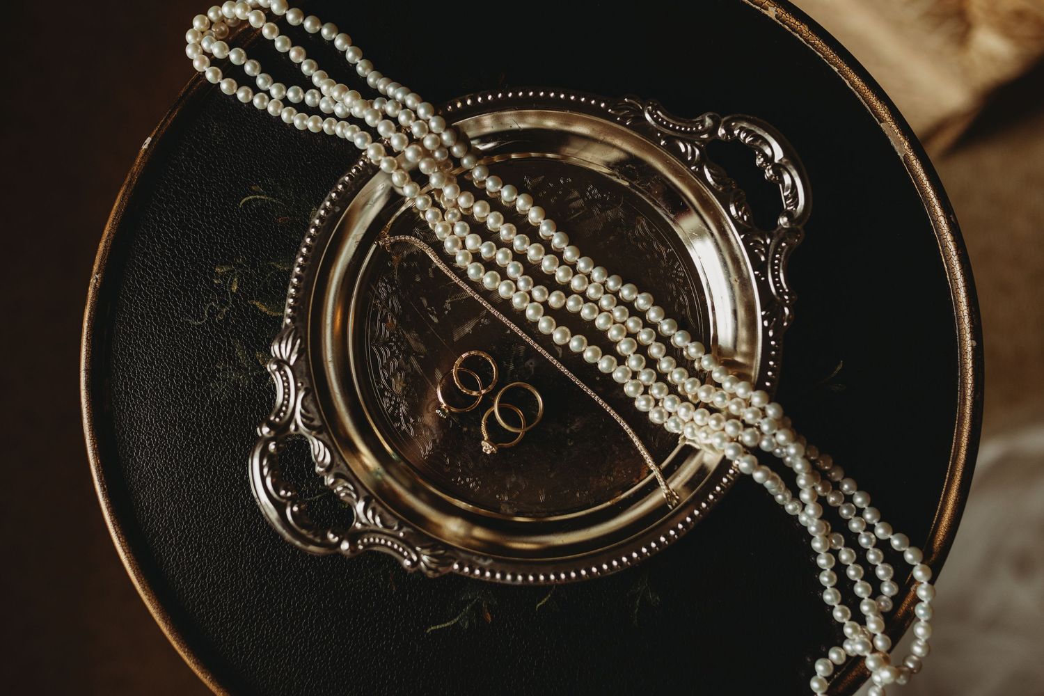 Pearl necklace and wedding rings displayed on an ornate silver tray.