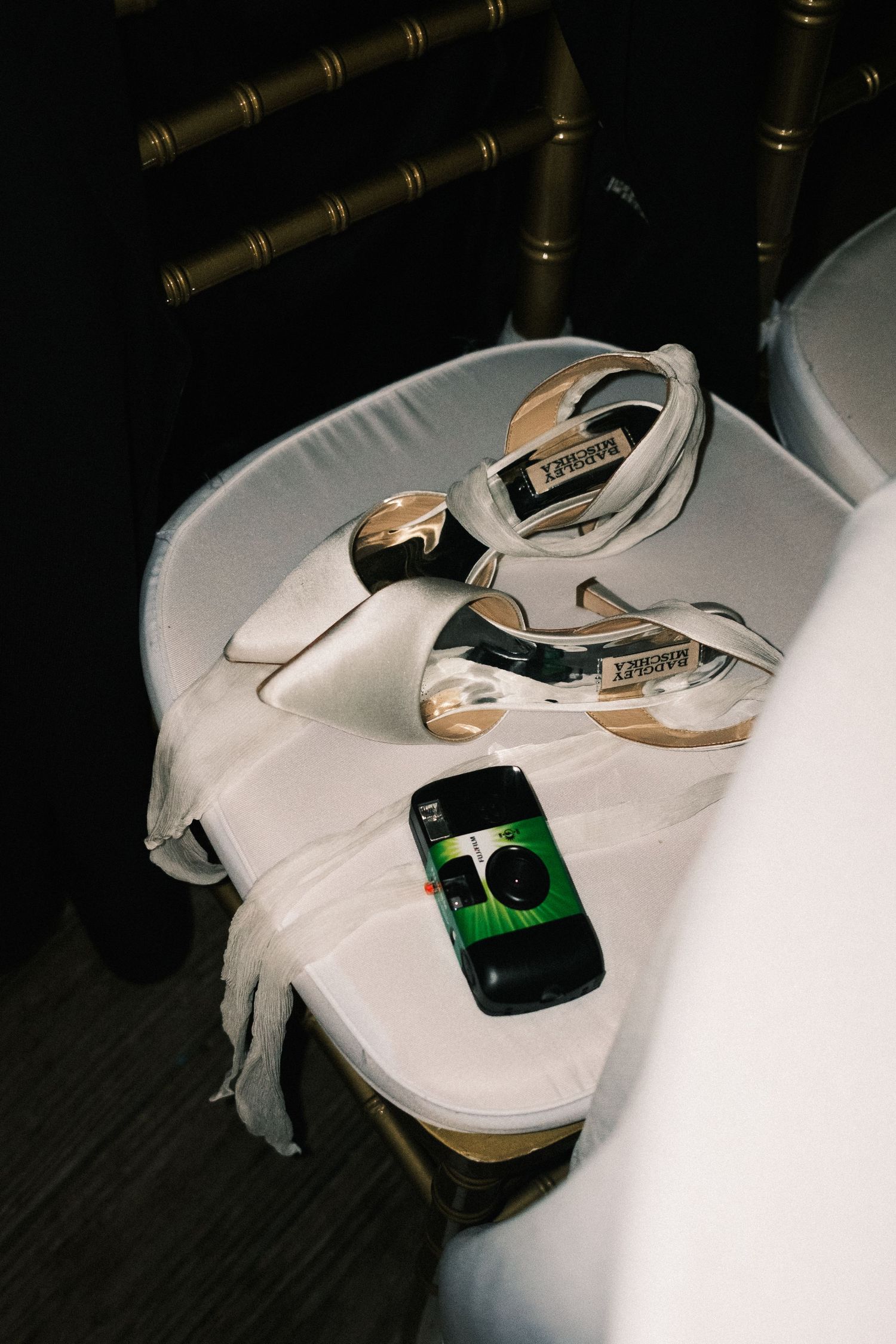 White bridal shoes and camera displayed on dark surface.