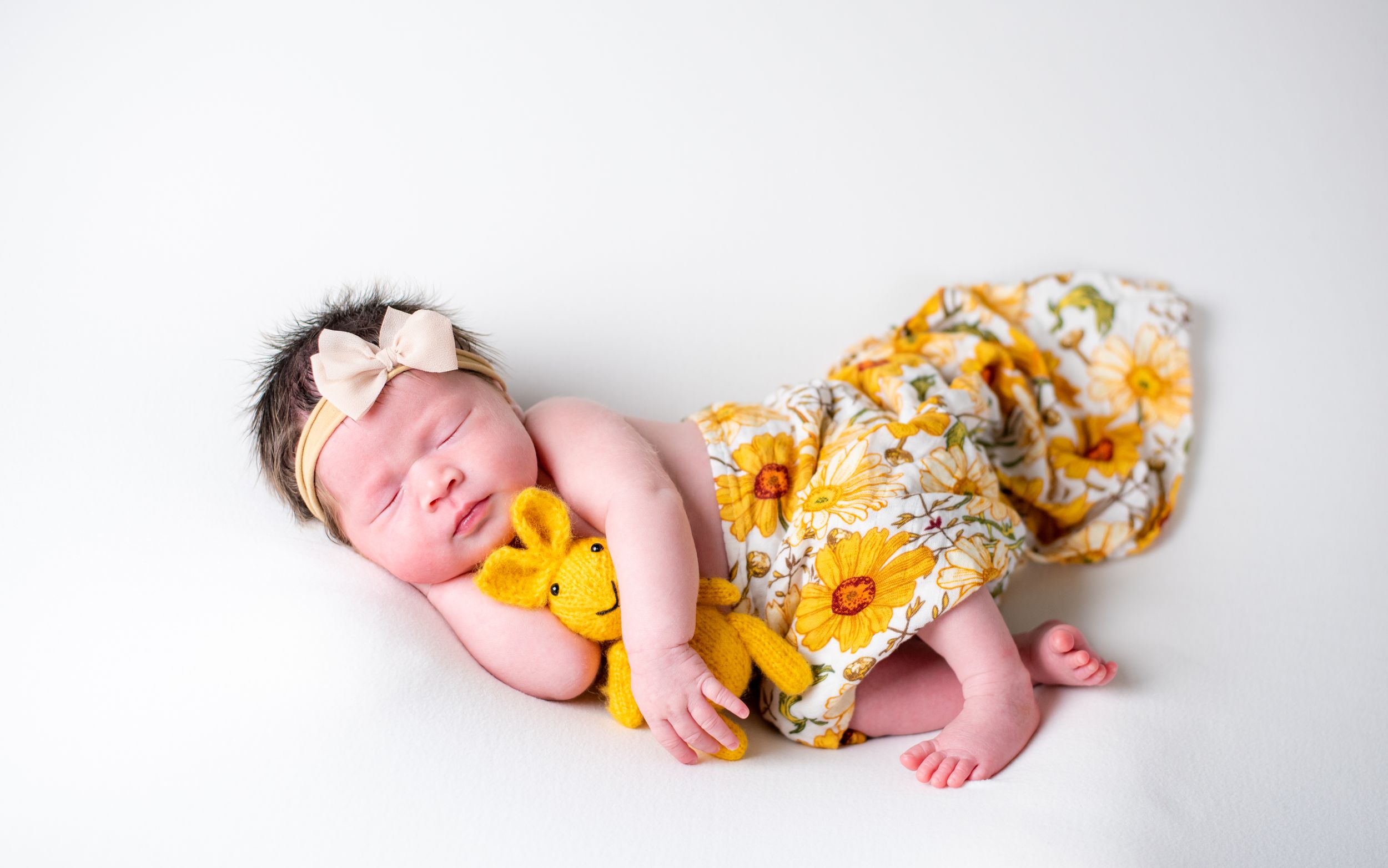 Sleeping newborn posed with sunflower print blanket on white background.