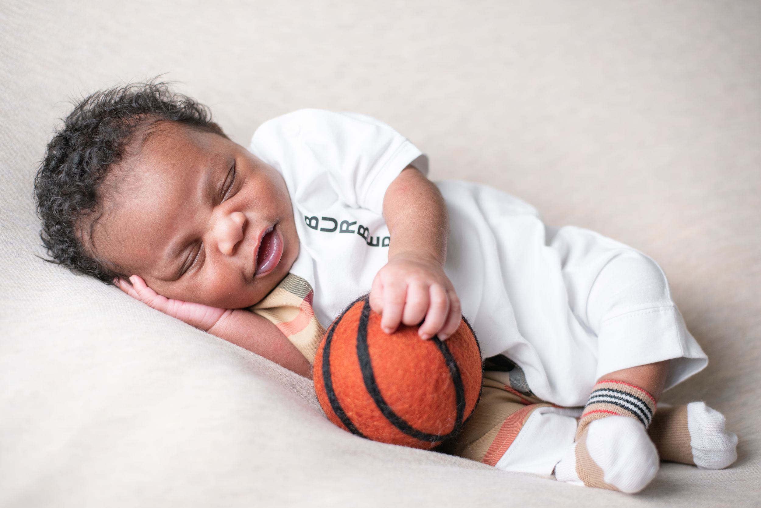 Sleeping newborn baby cradled with a small basketball in white onesie.