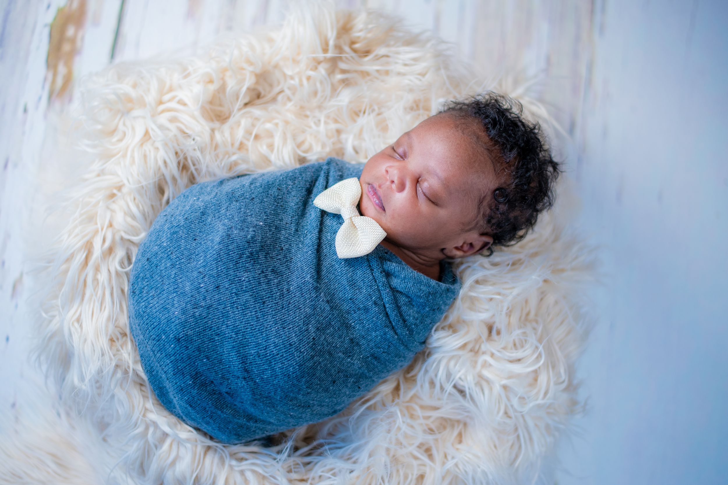Peaceful newborn baby wrapped in blue blanket sleeping on fluffy white fur.