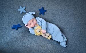 A sleeping baby wearing blue pajamas lies on grey carpet surrounded by star decorations.