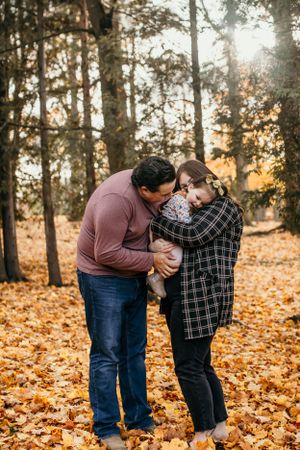Family sharing intimate moment together in autumn forest covered with fallen leaves.