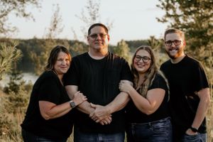 Group portrait of four people linking arms outdoors.