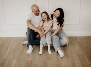 A joyful family sitting together on hardwood floor wearing casual white and gray outfits.