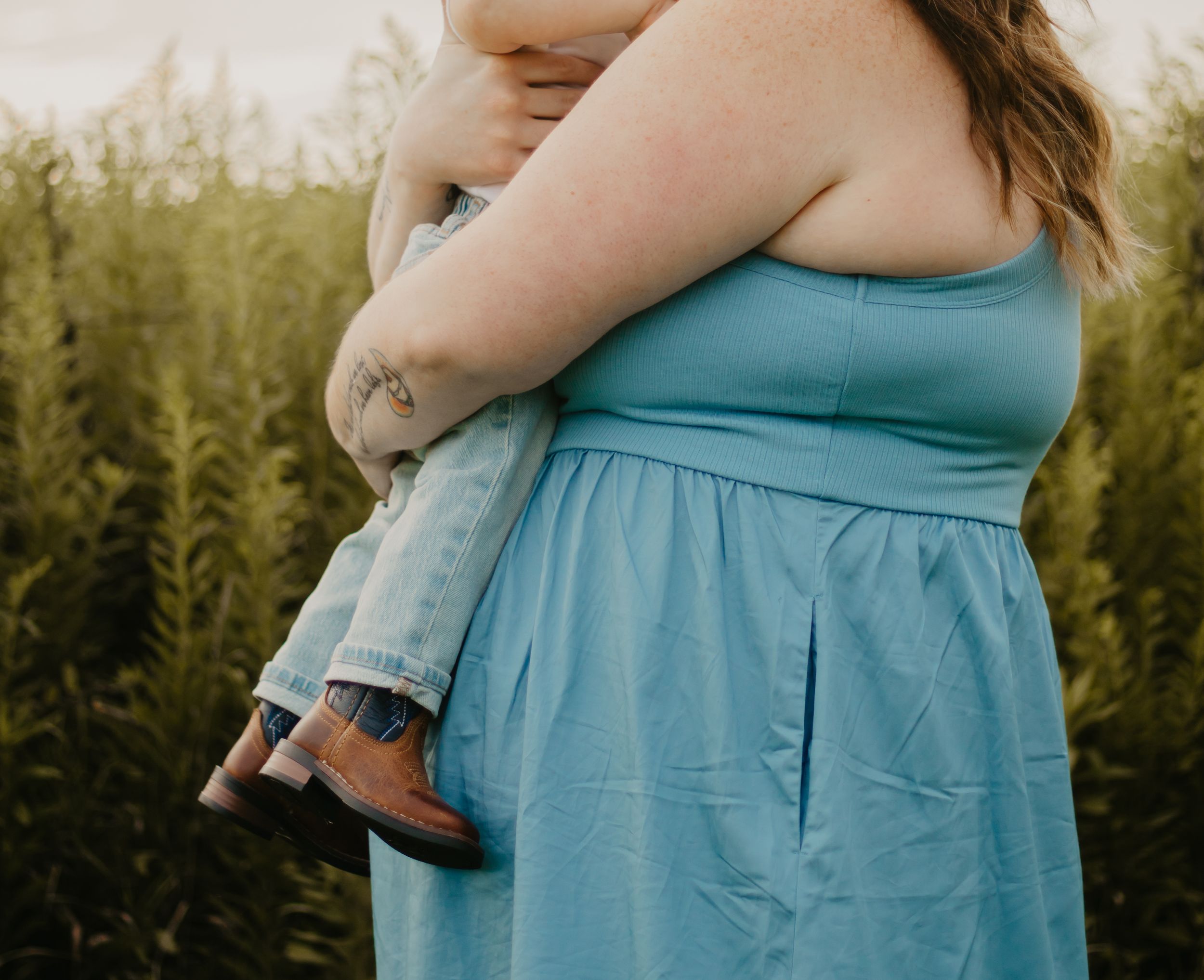 Parent holding small child against blue dress in outdoor setting.