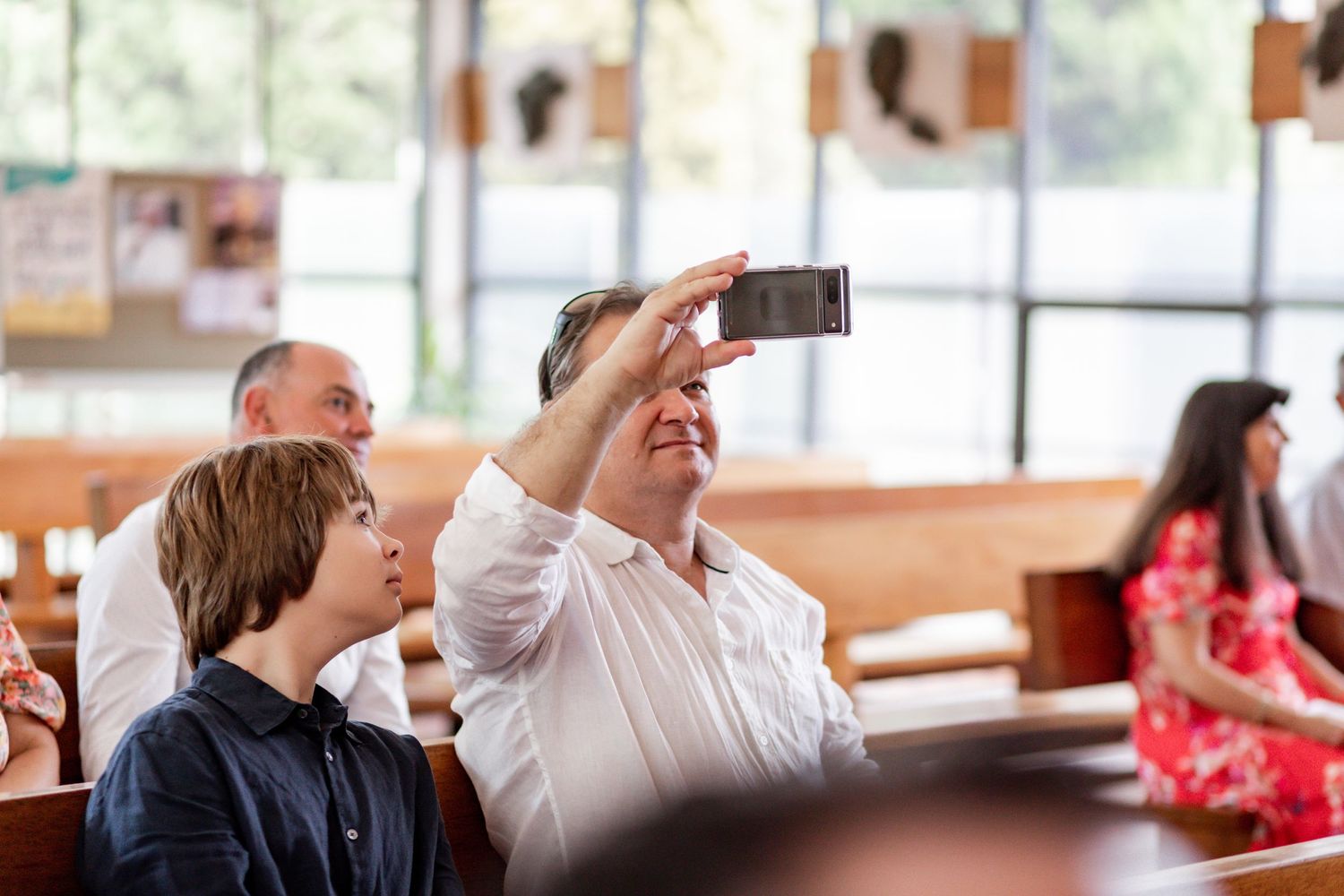 Church attendee takes photo with phone during religious ceremony while others watch.