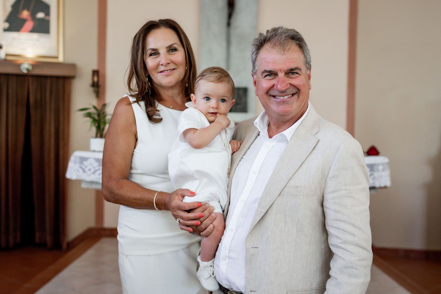A small group in white and beige formal attire pose together in front of religious decor.