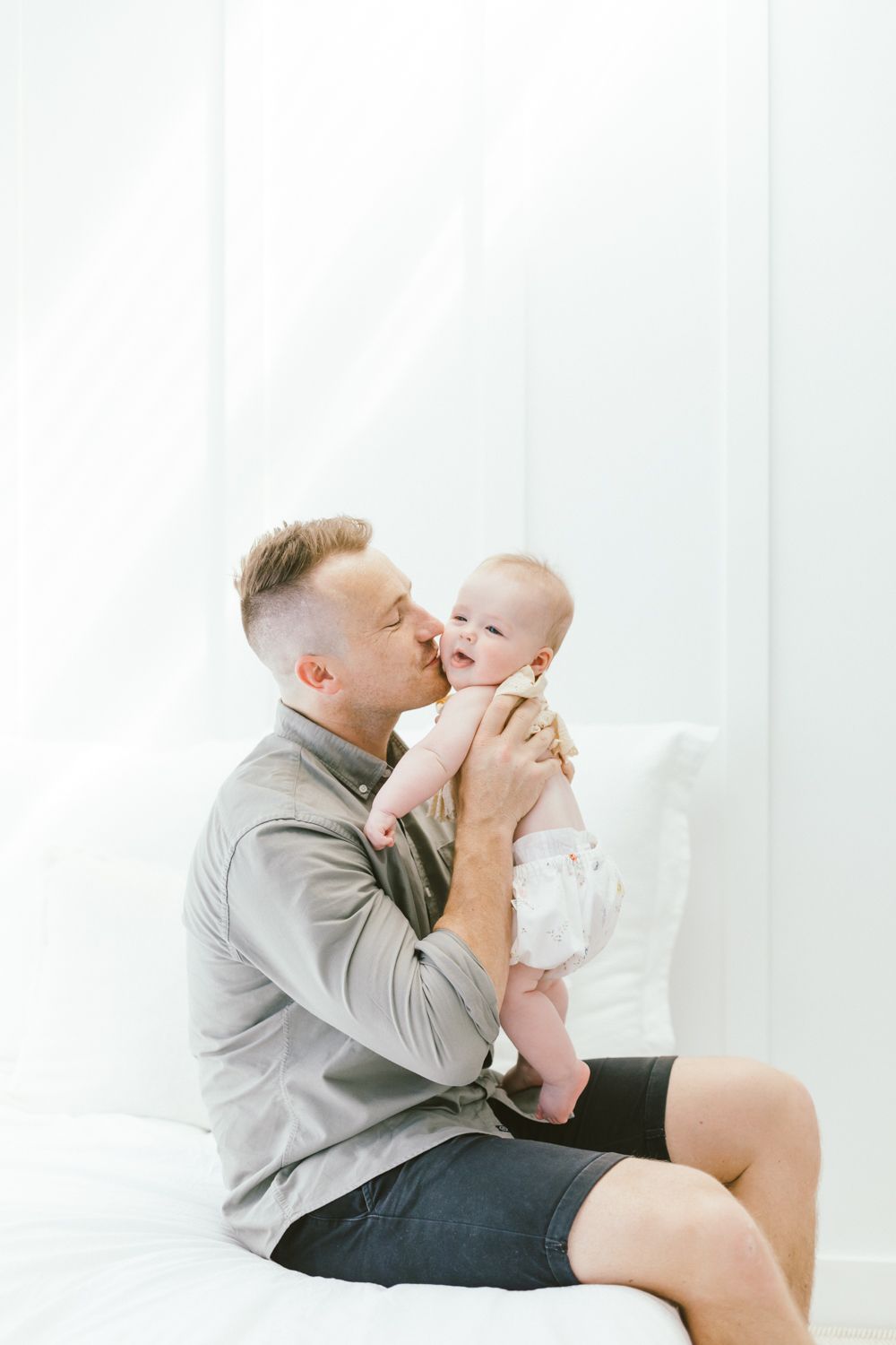 Tender moment between parent and baby during bright indoor photoshoot.