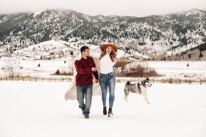 Happy Couple smiling and running with their dog in the snow covered mountains