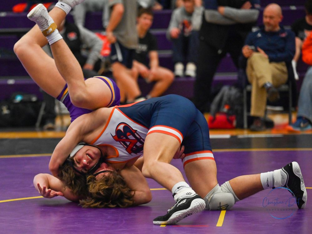 High school wrestlers competing in an intense match on a purple mat.