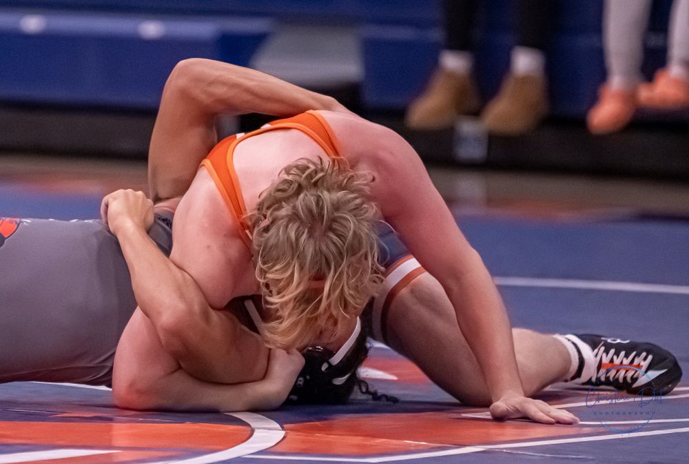 Two athletes in a wrestling match grappling on a red and blue mat.