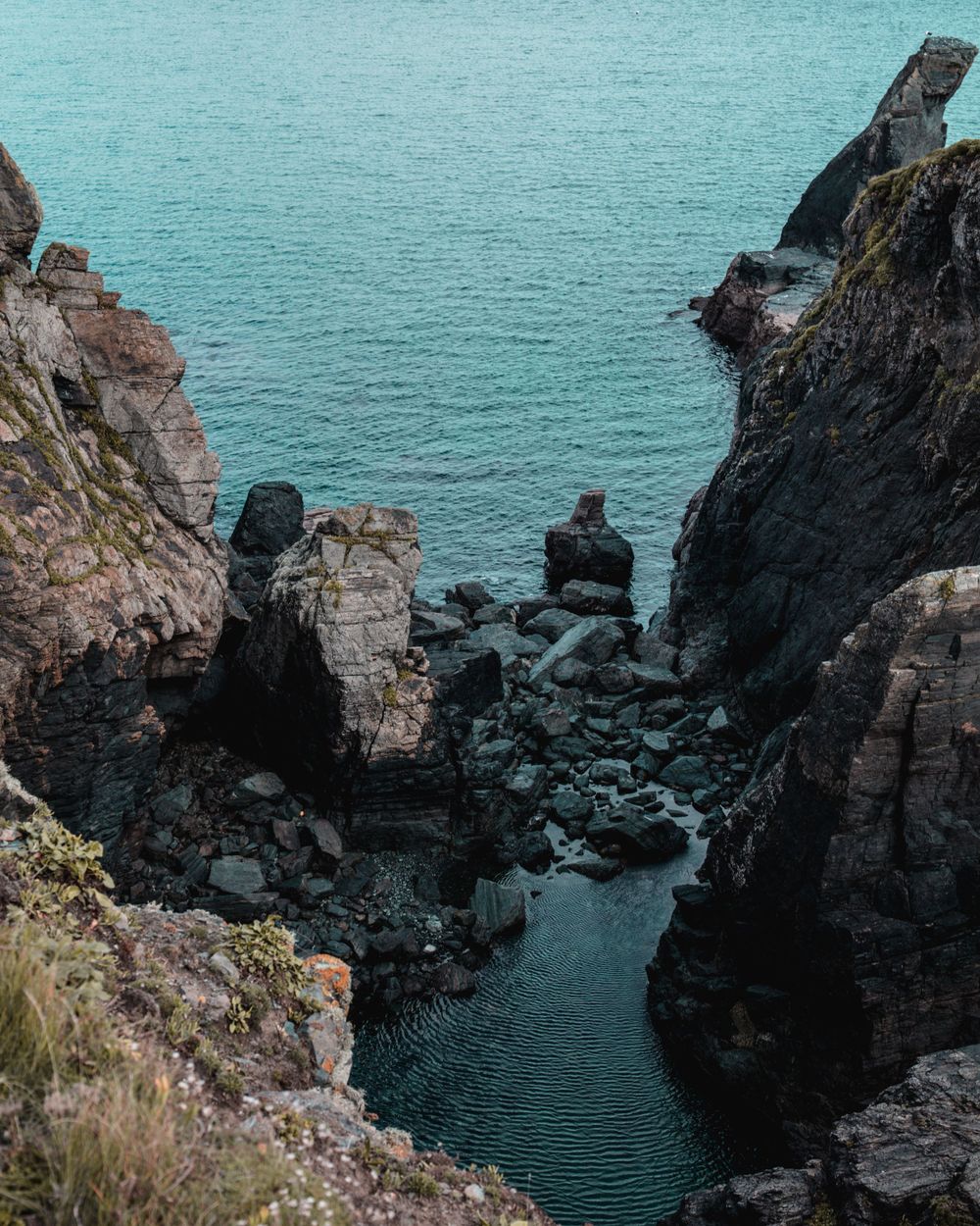 Dramatic rocky cove with turquoise water between steep cliffs and boulders.