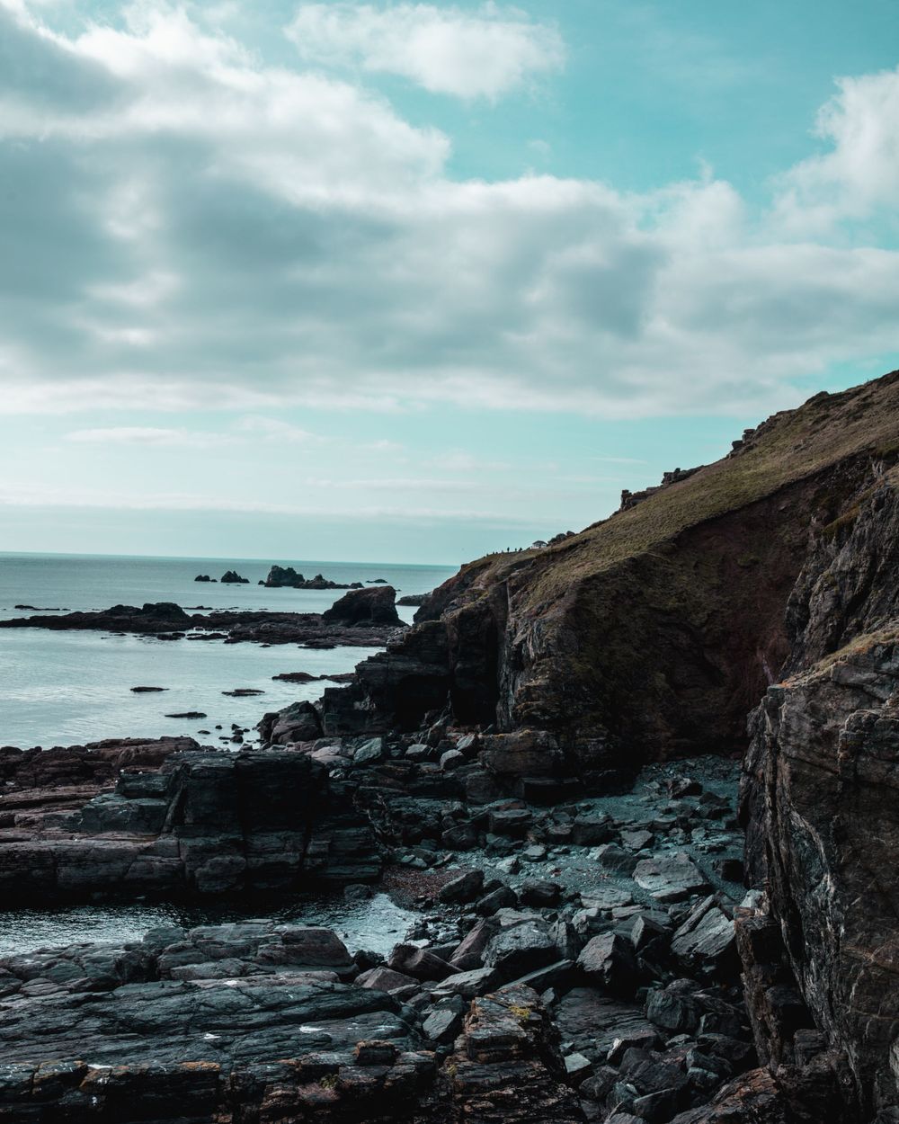 Rocky coastal cliffs meeting the ocean under a cloudy sky with waves crashing against the shore.
