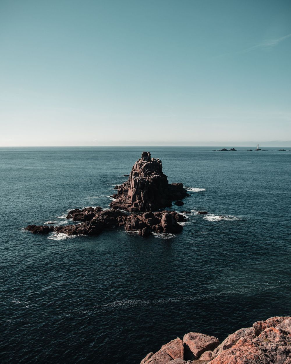 Isolated rocky sea stack formation rising from deep blue ocean waters against clear sky.